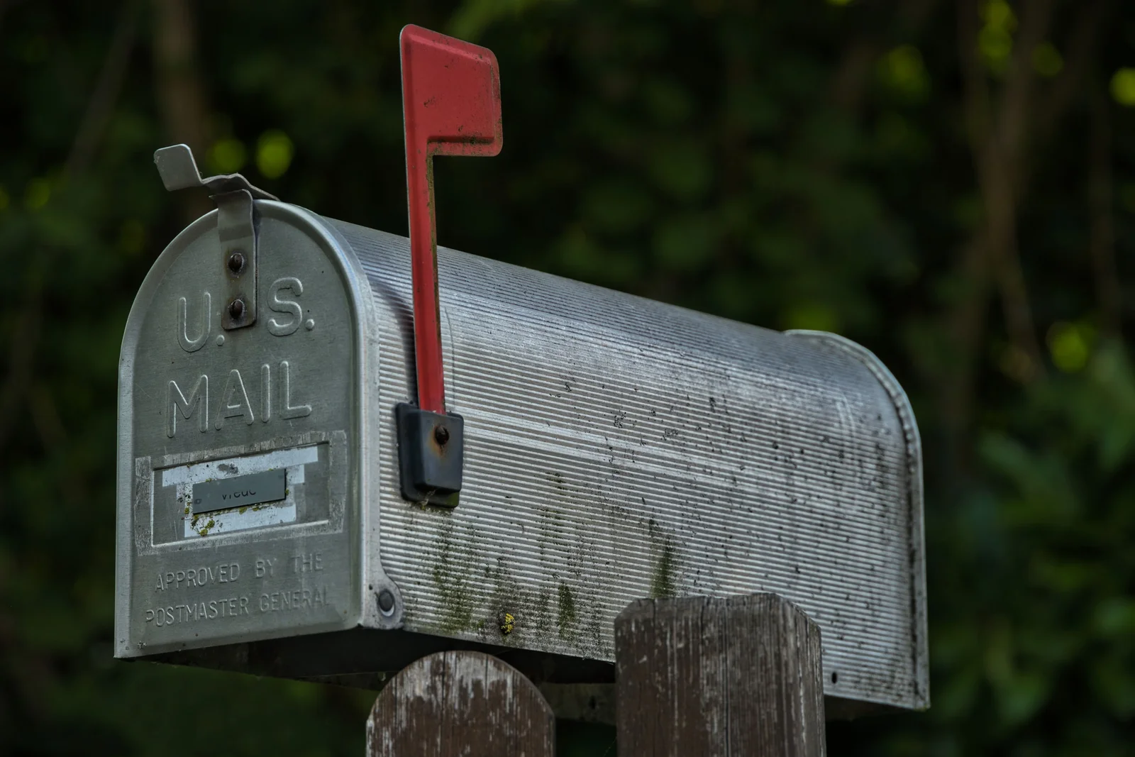 A weathered aluminum U.S. Mail box on a wooden post, red flag raised